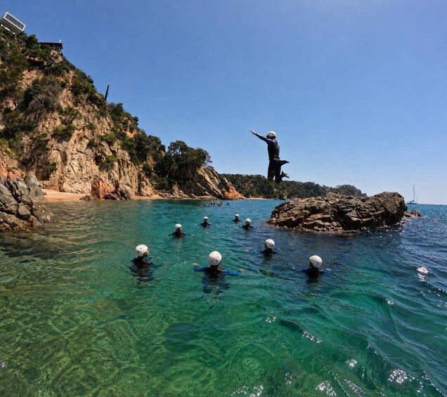 Divers in clear water near a rocky coastline with a person standing on a rock. 4