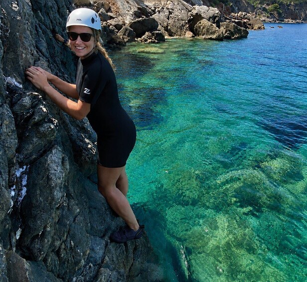 A person climbing a rocky cliff by a clear blue sea. 2