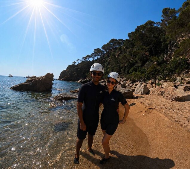 Two people standing on a beach with clear water and rocky cliffs in the background. 5