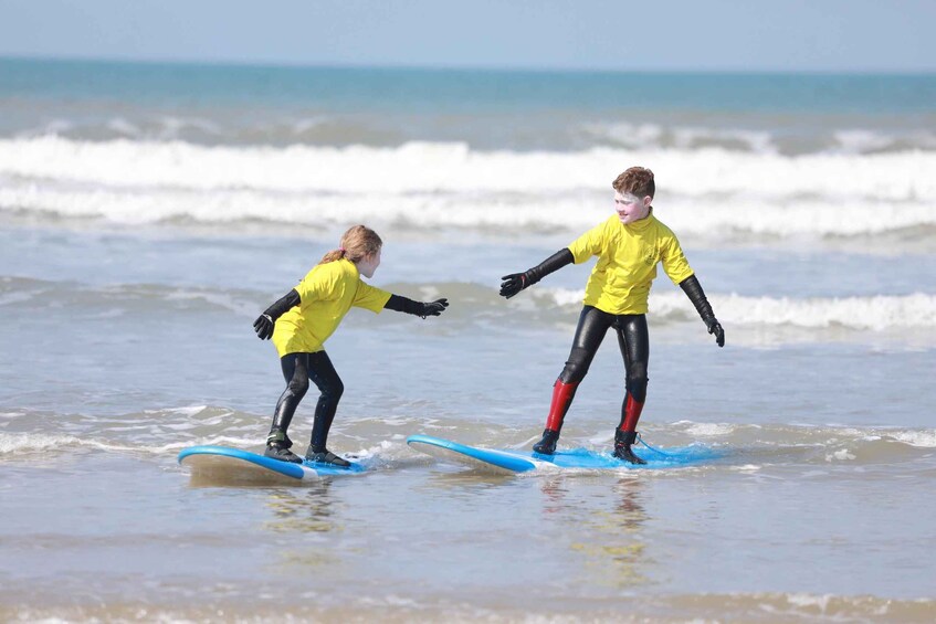Two people in yellow wetsuits surfing on a beach. 3