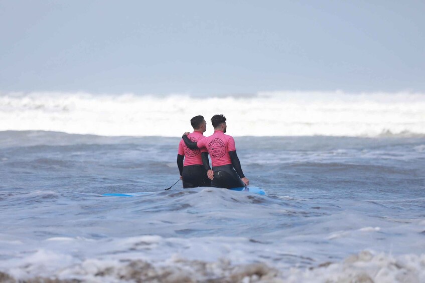 Two people in pink wetsuits sitting on surfboards in the ocean. 2