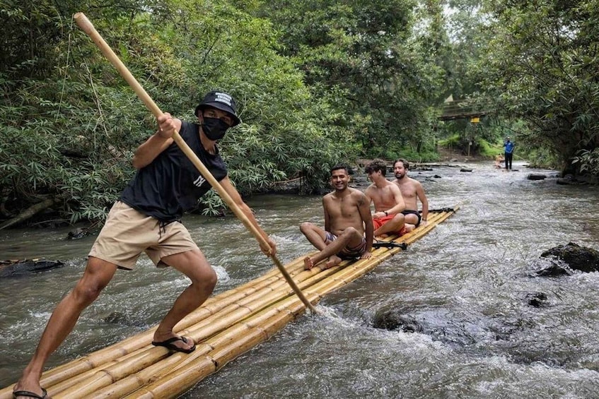 A group of people paddling on a bamboo raft in a river surrounded by dense greenery. 4