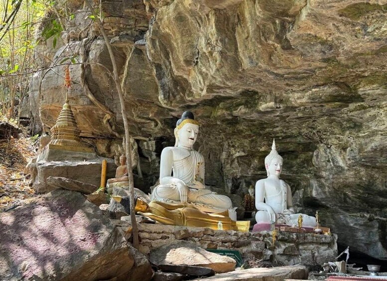 Two large white Buddha statues in a cave setting with a small stupa and various ritual items. 3