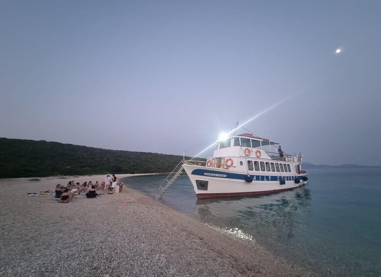 A boat named 'GIONIAN STAR' docked at a pebbled beach with people gathered on the shore. 5