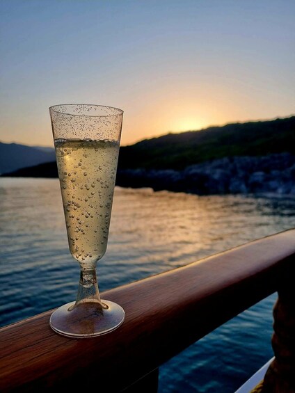 A glass of water on a wooden railing by a body of water at sunset. 2