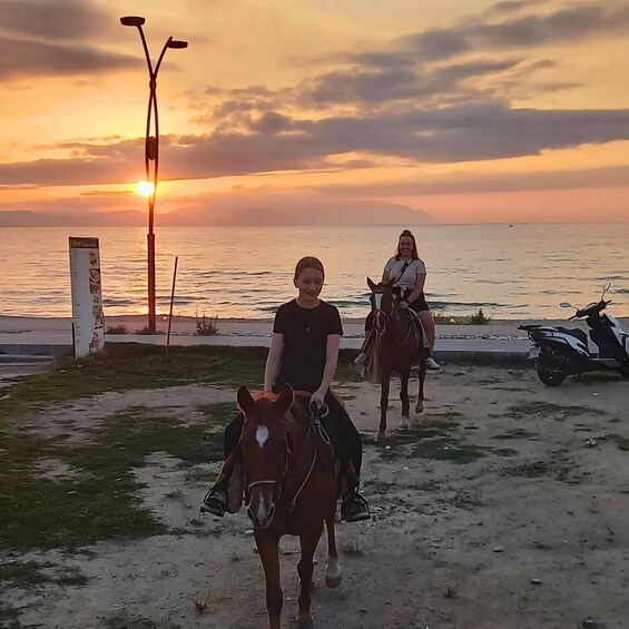 Two people riding horses on a beach at sunset. 3