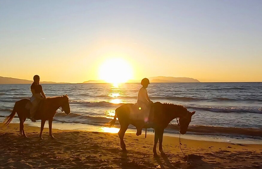 Two people riding horses on a beach at sunset. 1