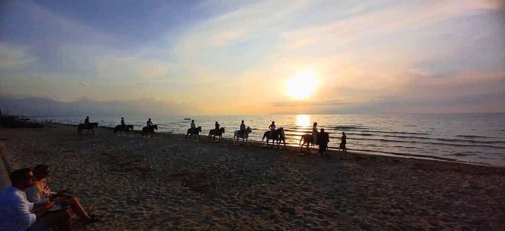 A beach with people riding horses along the shore during sunset. 5