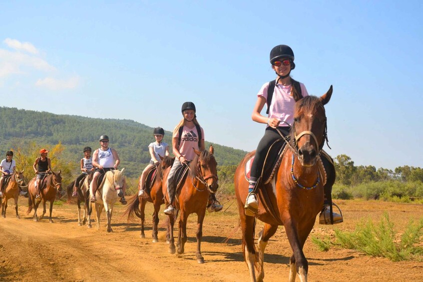 A group of people riding horses on a dirt path with a hilly landscape in the background. 4