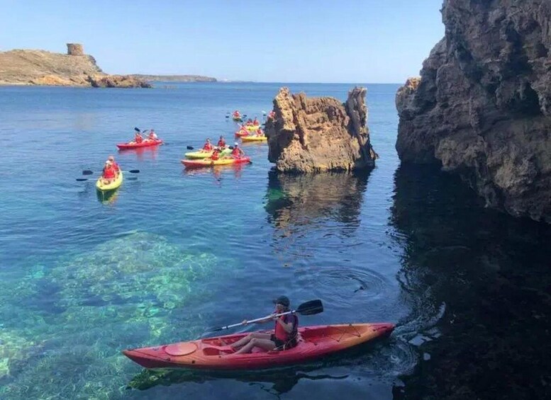 Kayakers on a calm sea, surrounded by rocky cliffs and clear water. 1