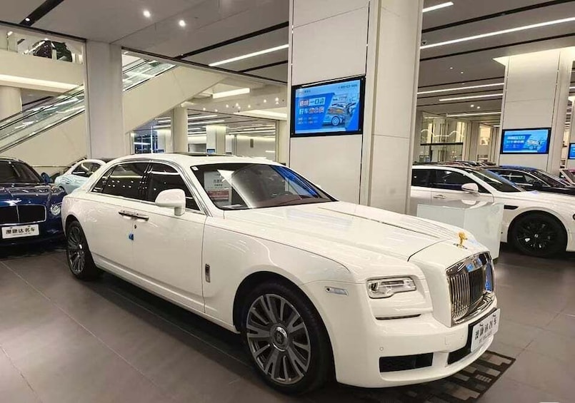A white luxury car in a showroom with digital displays and escalators. 4