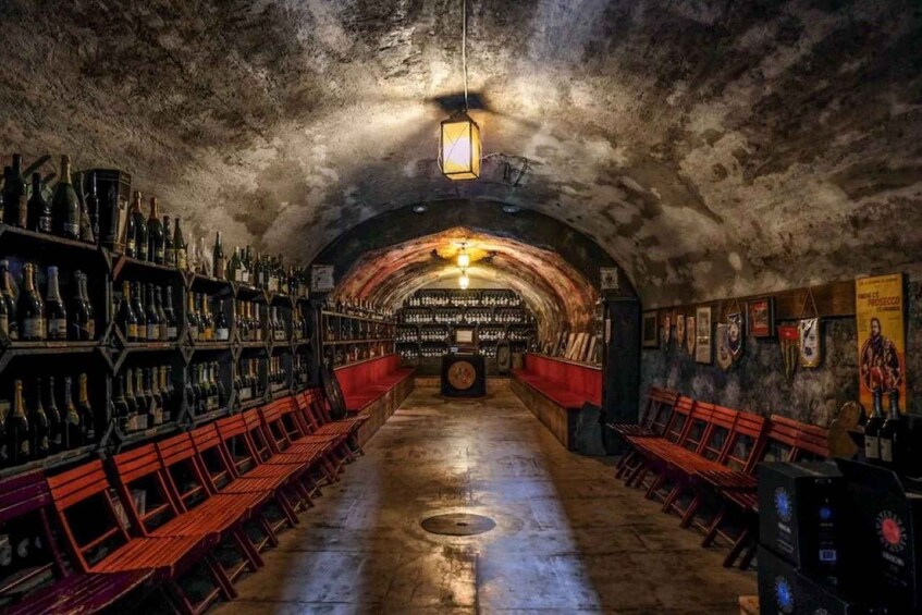 An underground bar with wooden benches and shelves of bottles. 5