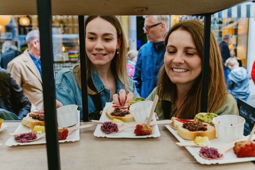 Two people sitting at a table with food, including sandwiches and small containers of sauces. 3