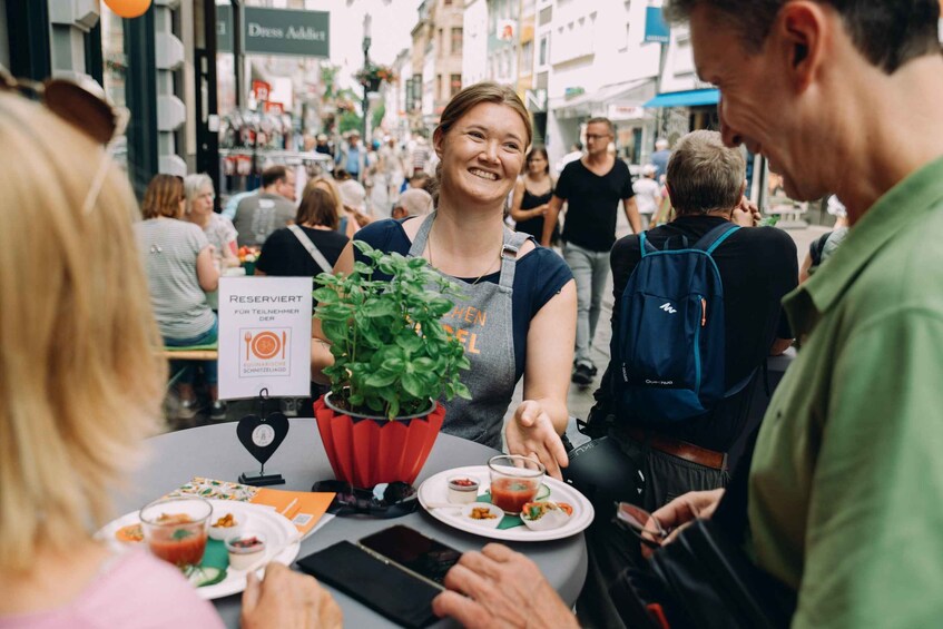 A person seated at a table with a potted plant, a menu, and a smartphone. 1