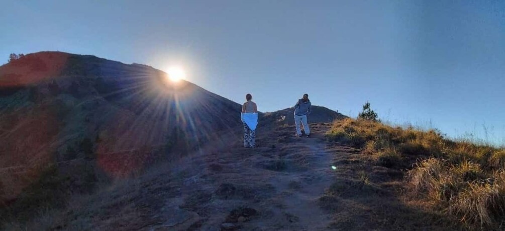 Two people hiking on a dirt trail with the sun setting in the background. 1