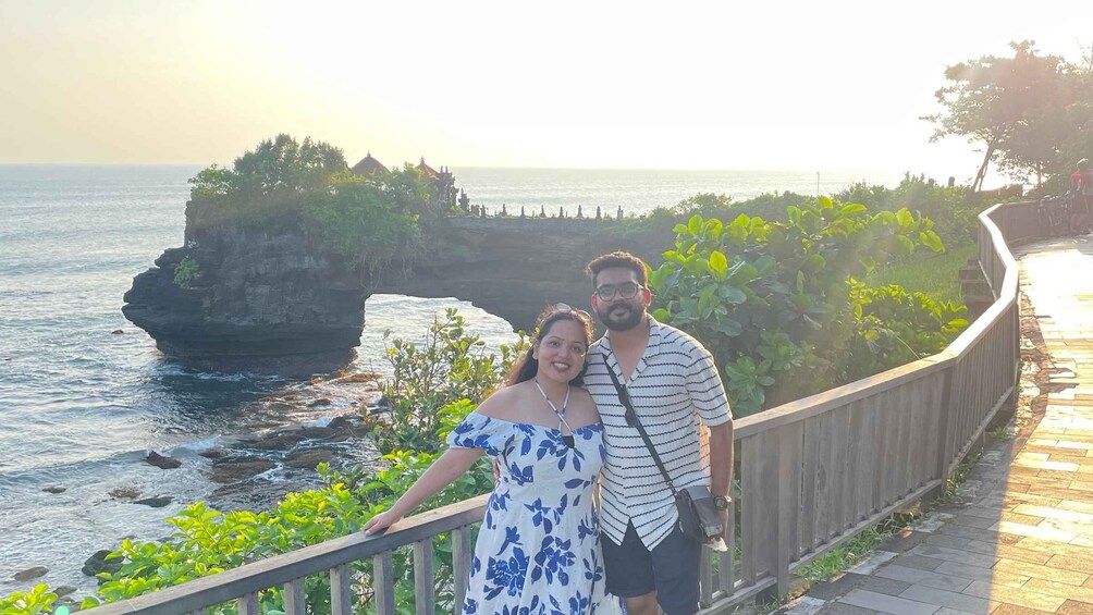 A couple standing on a wooden boardwalk overlooking a coastal cliff with a view of the ocean. 2