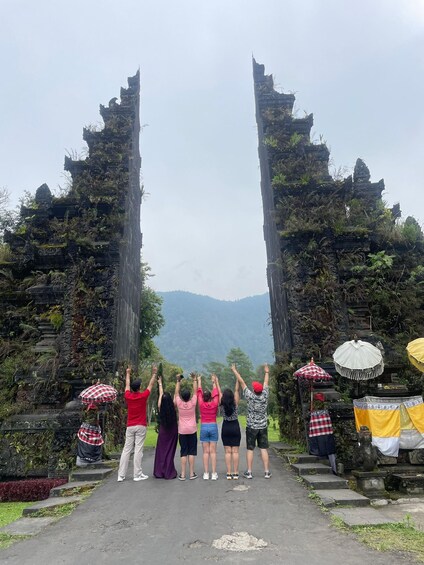 A group of people standing at an ancient stone gate with their hands raised, overlooking a mountainous landscape. 4
