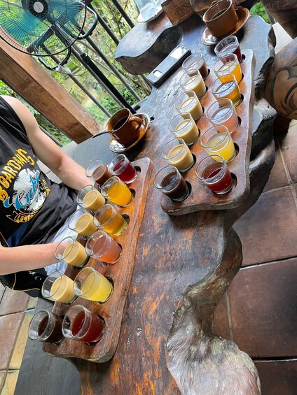 A wooden table with multiple glasses of beverages, a cup, and a smartphone. 2