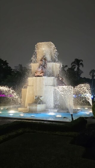 A nighttime fountain with water jets and a statue. 4