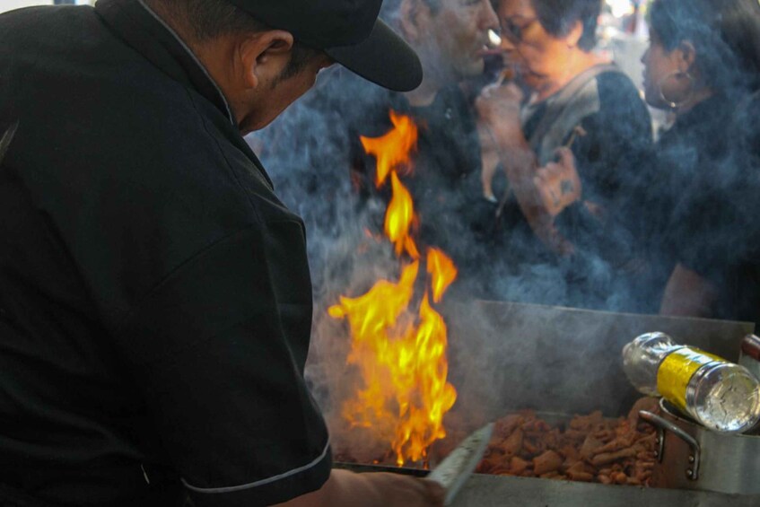 A person grilling sausages over an open flame, with a bottle of cooking oil nearby. 1