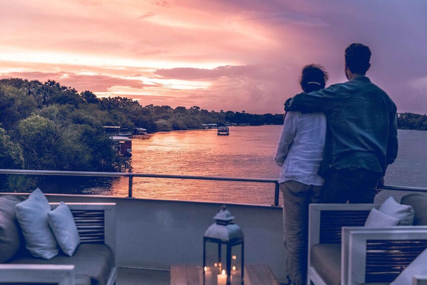 A couple embracing on a balcony overlooking a river at sunset. 1