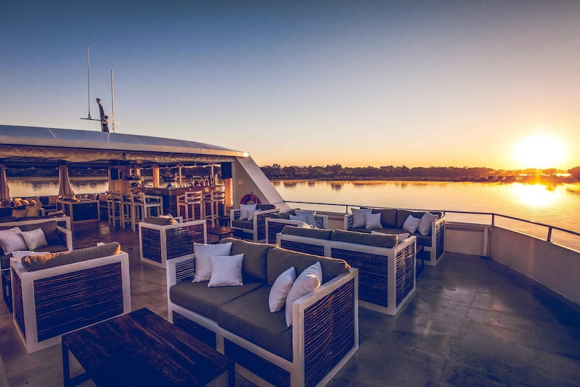 A sunlit deck with outdoor seating and a view of a calm body of water at sunset. 5