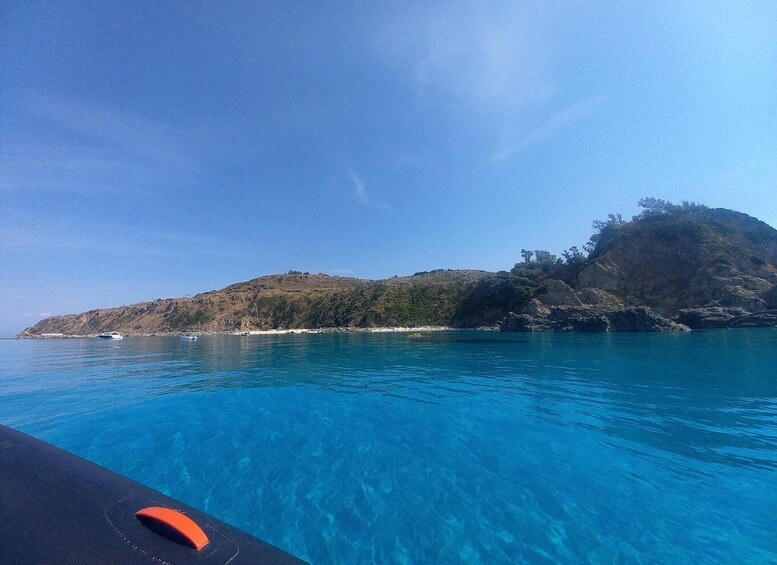 A clear blue sea with a boat in the foreground and a hilly landscape in the background. 5