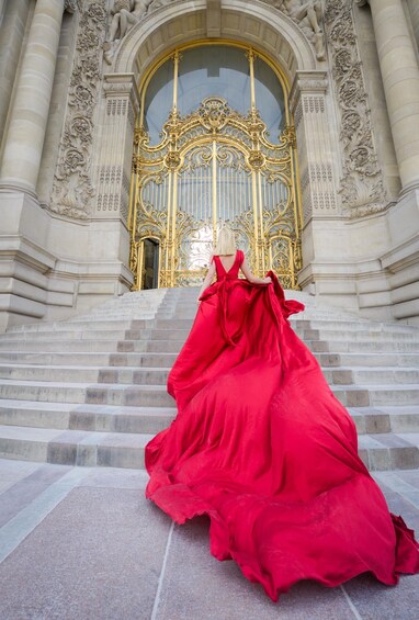 A person in a red dress descending a grand staircase with ornate gold doors and classical architecture. 2