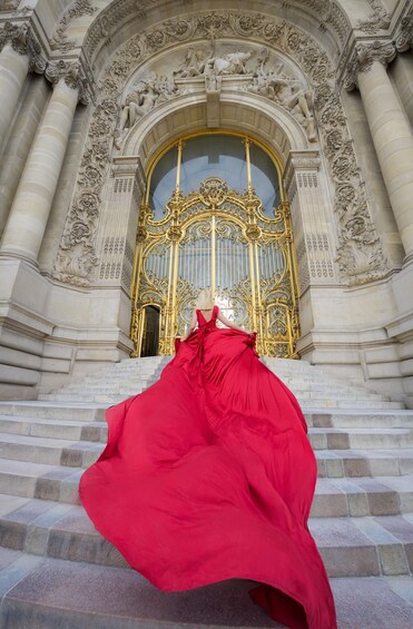 A person in a red dress descending a grand staircase with ornate architecture and a golden door. 4