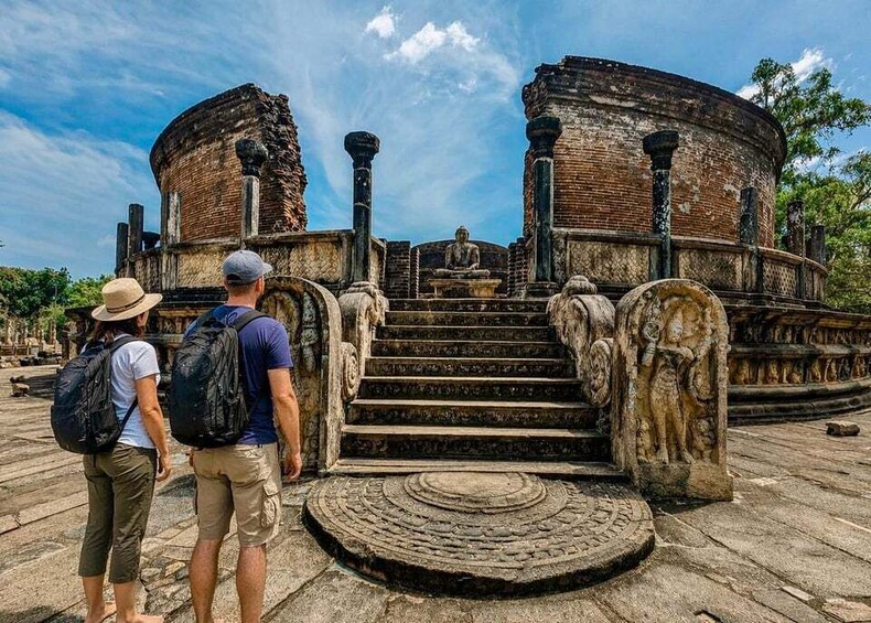 A historical site with ancient brick structures and stone steps leading to a central area with a seated figure. 1