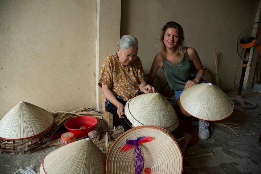 Two people working with woven conical hats, surrounded by materials and tools. 4