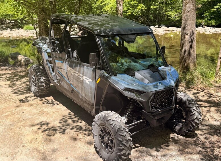 A Polaris RZR off-road vehicle parked by a calm river with trees in the background. 4