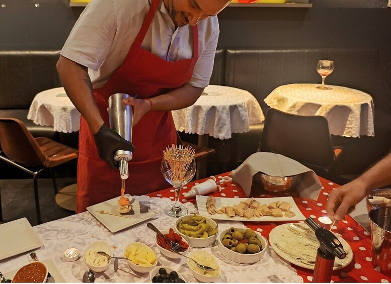 A person in a red apron preparing food at a table with various dishes and a wine glass. 3