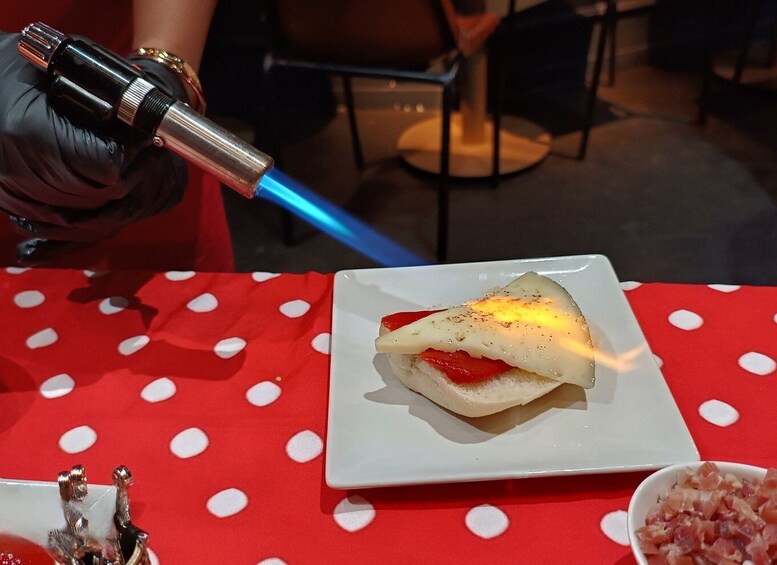 A person holding a blowtorch over a dish on a red tablecloth with white polka dots. 1