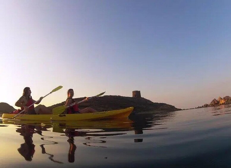 Two people kayaking on calm water with a hill and a tower in the background. 2