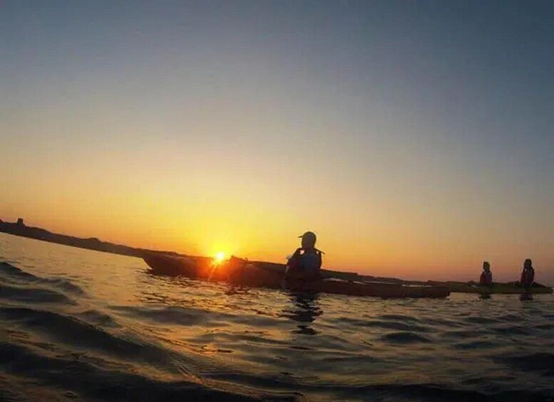 A sunset over a calm body of water with a boat and people on the shore. 1