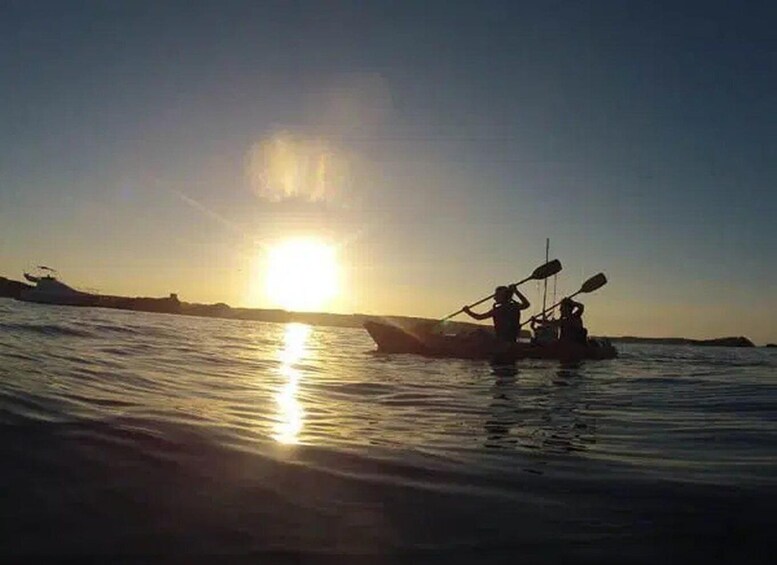 A sunset over calm waters with a small boat and two people paddling. 5