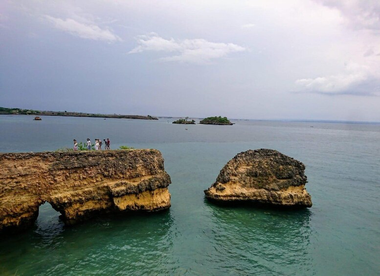 A coastal landscape with rocky formations and a group of people standing on a cliff overlooking the water. 5