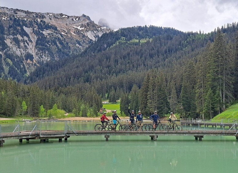 A group of cyclists on a bridge over a lake with mountains in the background. 1