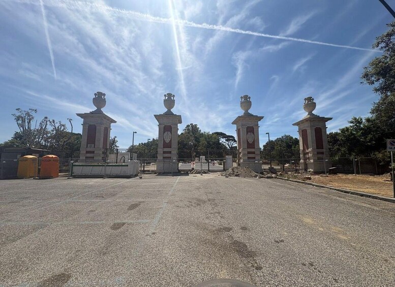 A paved area with four statues, a clear sky, and trees in the background. 5