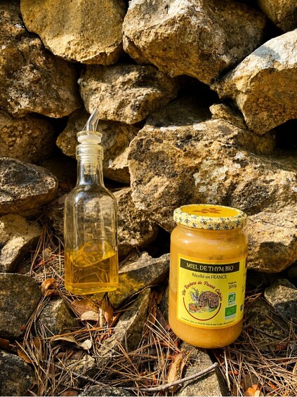 A bottle of Miel de Thym Bio honey and a jar of honey in a rocky outdoor setting. 4