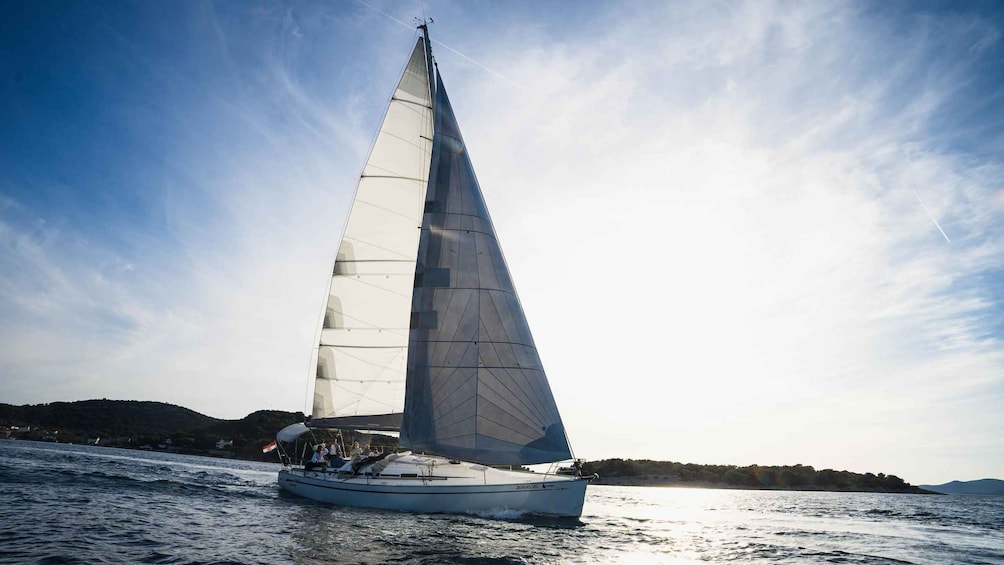 A sailboat with a large sail on a body of water, surrounded by a hilly landscape. 1