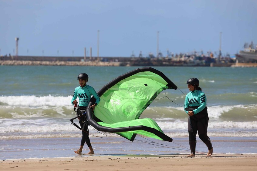 Two people walking on a beach with a large green kite. 2