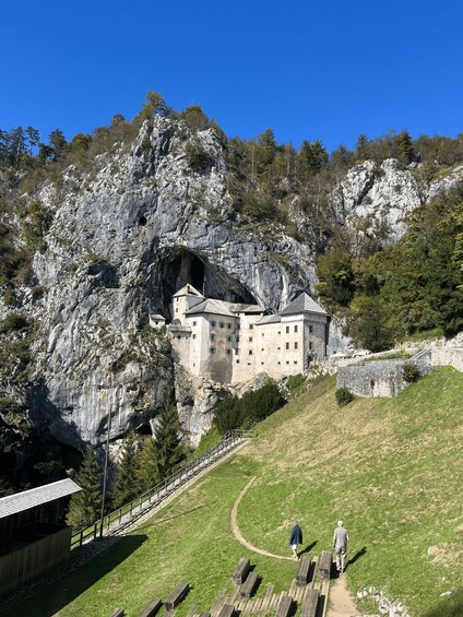 A castle built into a rocky cliff, with a path leading to it and two people walking. 1