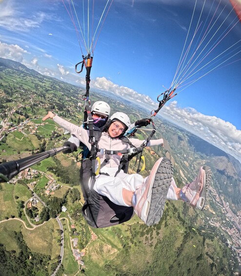 Two people paragliding over a landscape with houses, roads, and mountains. 1
