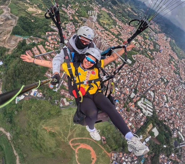 Two people paragliding over a cityscape with buildings and greenery below. 4