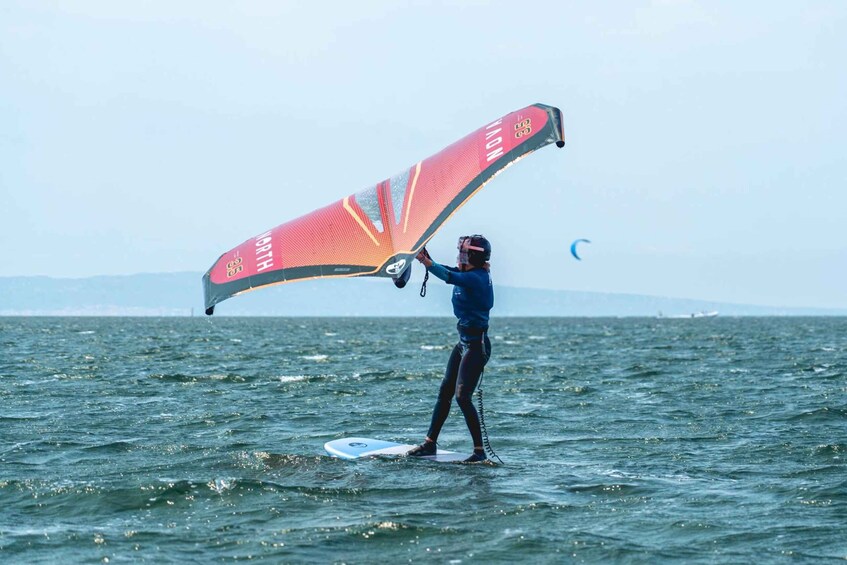 A person windsurfing on a body of water with a red sail. 1