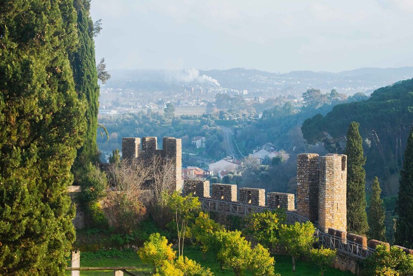A historic stone fortress with battlements, surrounded by lush greenery and overlooking a valley with a distant cityscape. 3