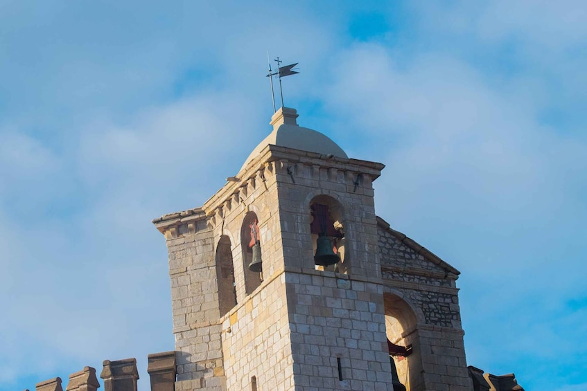 A stone bell tower with a weather vane, arched windows, and a dome. 1
