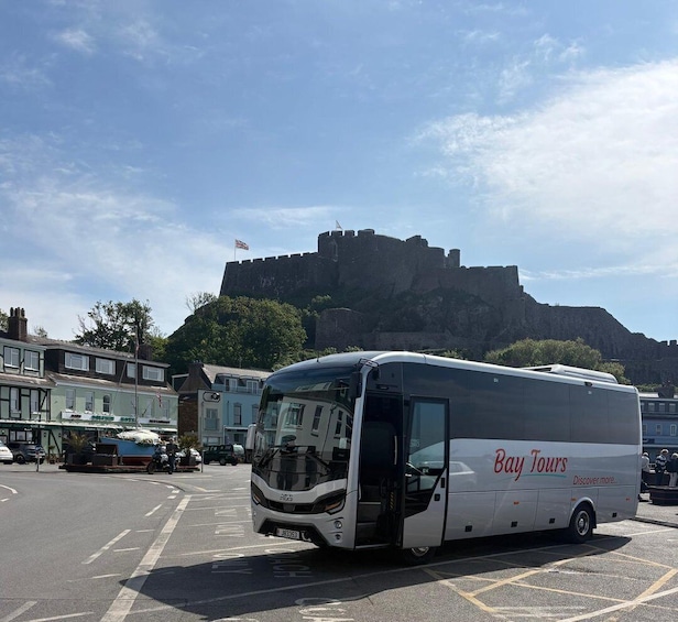 A white tour bus with 'Bay Tours' branding parked in a lot with a historic castle in the background. 1